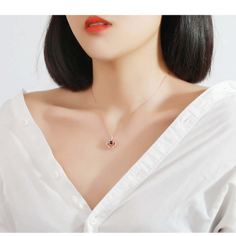 A women wearing a rose gold color I love you necklace with 100 different languages. The Women is wearing white top with a red lipstick. 